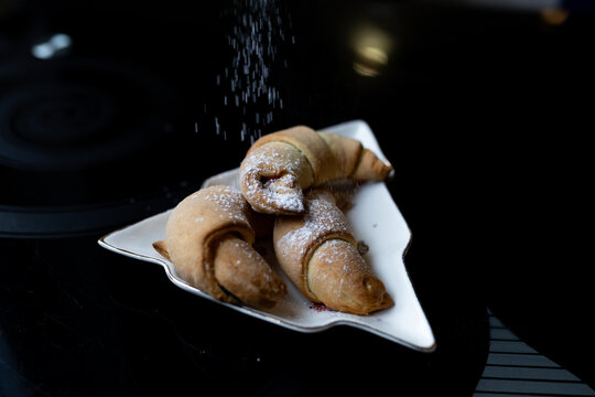 Close-up view of croissants being sprinkled with powdered sugar. Falling sugar highlights the fresh pastry texture in a simple bakery scene - Powered by Adobe