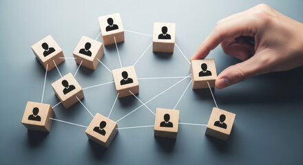 Hand places wooden block with a person icon, completing a connected network on a gray backdrop. Illustrates business connections, team building, and human resources concepts.