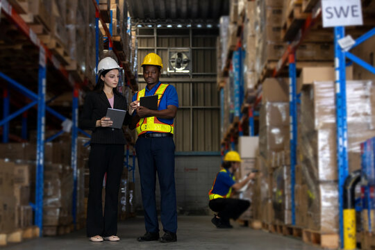 Warehouse supervisor and worker using digital tablets to review logistics data while another staff scans package. Concept of warehouse coordination, inventory tracking, smart supply chain operations.