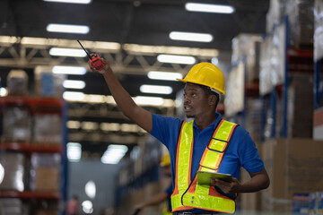 Warehouse worker in safety vest and helmet using walkie-talkie and tablet to coordinate inventory movement. Concept of logistics communication, supply chain operation, warehouse efficiency.