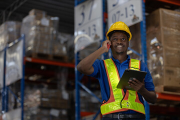 Smiling warehouse man worker in safety vest using mobile phone and digital tablet for communication and inventory coordination. Concept of smart logistics, operation, real time management.