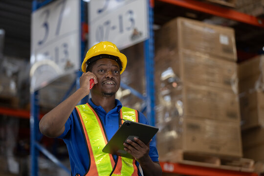 Smiling warehouse man worker in safety vest using mobile phone and digital tablet for communication and inventory coordination. Concept of smart logistics, operation, real time management. - Powered by Adobe