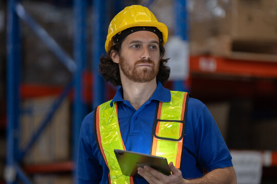 Confident warehouse worker in safety gear holding digital tablet while monitoring operations. Concept of modern logistics, inventory control and warehouse management with smart technology.