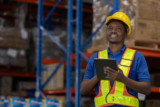 Smiling warehouse worker in safety uniform using digital tablet to monitor inventory in storage facility. Concept of smart logistics, inventory tracking and efficient warehouse management. - Powered by Adobe