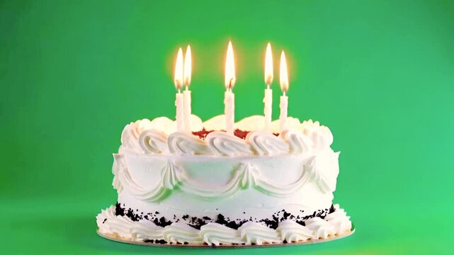 A birthday cake with white lit candles on a green screen.