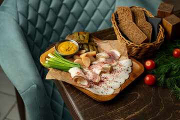 A delightful assortment of cured meats is arranged on a wooden platter, complemented by pickled vegetables and fresh greenery. Rustic bread adds to the hearty ambiance