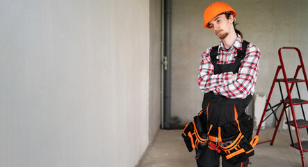 Tired sad male laborer, builder or repairman wearing helmet and tool belt ready for repairing or...