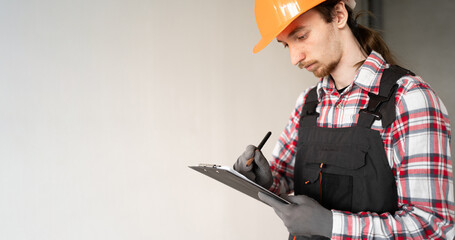 Young male builder writing notes on clipboard at construction site