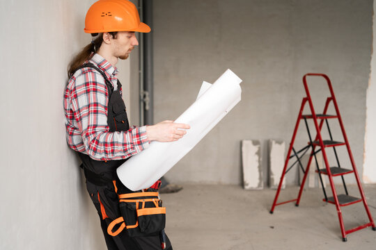 Male Construction worker wear hard hat reading blueprints inspecting building site - Powered by Adobe