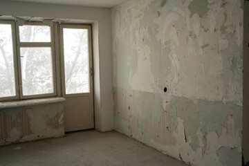 Old rundown apartment before renovation with peeling grey wall hanging in strips, cracked plaster walls, dusty wooden floor, empty and waiting for a new life