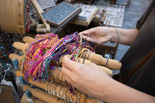 Female hands selecting colorful handmade thread bracelets on a wooden display, close view of craft jewelry in a shop, for fashion, retail, shopping, artisan craft, lifestyle, gift ideas.