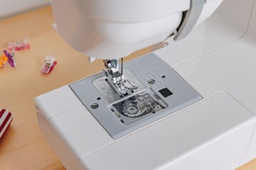 A Close-Up View of a Sewing Machine's Needle and Feed Dogs on a Minimalist Work Surface with Crafting Materials in the Background