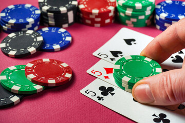 A player is focused on their hand in a poker game, placing a green chips next to three fives...