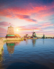 white windmill reflected in glassy river at sunrise with vivid pink and orange sky, twin mill silhouettes on horizon and smooth