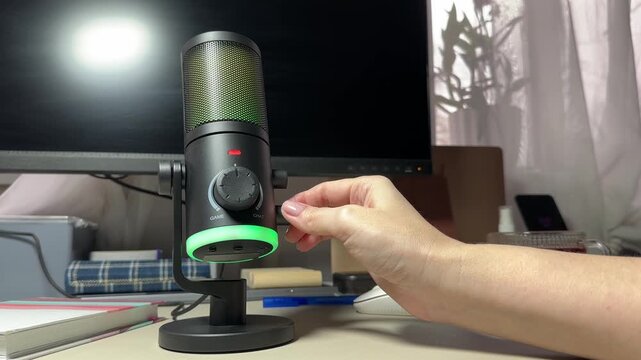 Female hand switching different modes on gaming microphone in front of desktop setup