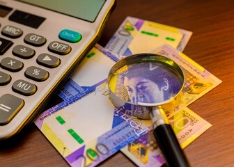 An overhead shot of Peruvian 200-sol banknotes, a calculator, and a magnifying glass on a wooden surface. It suggests themes of financial auditing, currency analysis, and accounting.