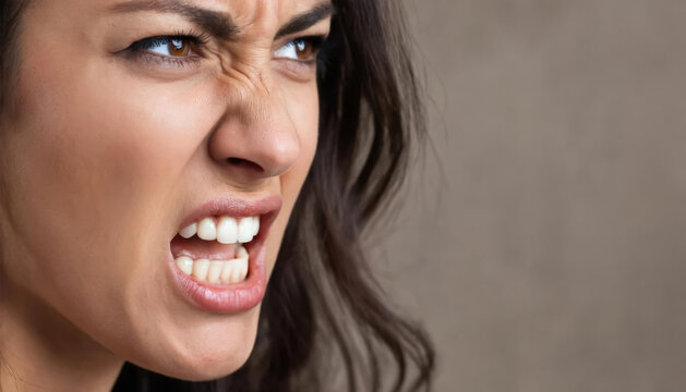 Close up of an angry woman showing aggression with furrowed brow and open mouth, expressing strong negative emotion.