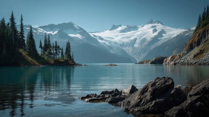 Bright sunlight illuminates a serene mountain lake surrounded by towering snow capped peaks and vibrant green trees. The water is calm creating beautiful reflections on the surface.