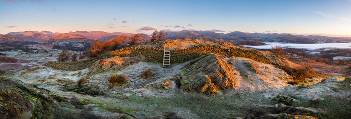 Panoramic view of frosty winter landscape with wooden stile over dry stone wall, Black Fell, Lake District, UK.