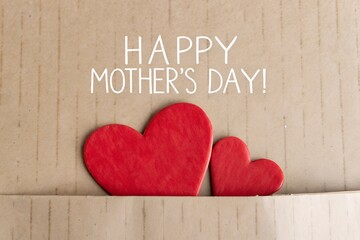 Two red hearts and happy mothers day text on a brown background