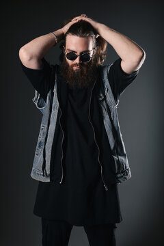 Studio fashion: handsome young man wearing jeans, denim coat and sunglasses (metalhead). Portrait of informal long-haired and bearded guy