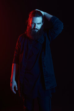 Studio fashion: handsome young man (metalhead). Portrait of informal long-haired and bearded guy in blue-red light