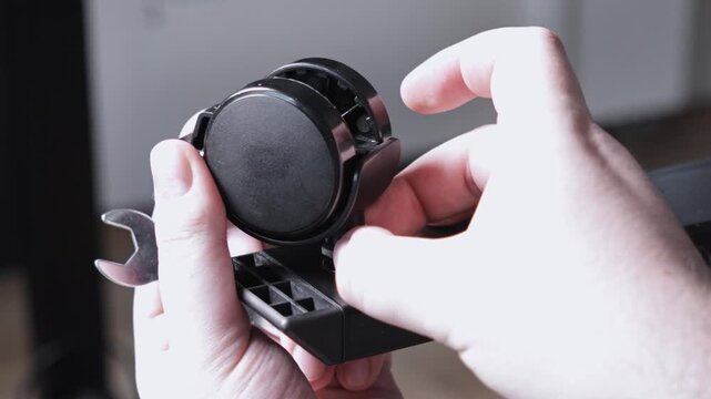 A person's hands are carefully attaching a durable black caster wheel onto a furniture base with a small metal wrench, demonstrating efficient home assembly