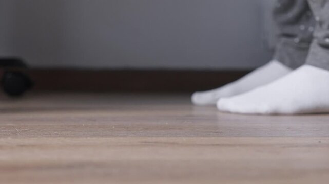 Black caster wheel on furniture offers silent mobility across a light wooden floor, with blurred human feet in white socks, indicating a comfortable home environment