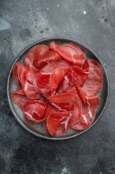 Lean marbled dried beef cecina arranged on a dark plate against a gray concrete surface, showcasing premium charcuterie texture.