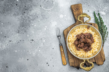 Kawurma qawurma layered over aromatic rice pilaf, highlighting seared protein fibers, granular structure and vintage culinary setup.