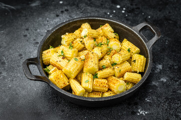 Golden fried baby corn pieces seasoned with spices and thyme served in cast iron skillet on black background top view
