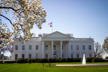 Obraz premium Whitehouse stands in Washington DC on a bright day with people visiting the grounds and the American flag flying high above