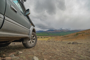 A rugged off-road vehicle on mud tires stands atop a rocky hill in the Altai, showcasing a stunning...