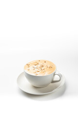  white cup filled with a foamy latte or cappuccino, topped with pine nuts or seeds, sitting on a saucer against a white background.