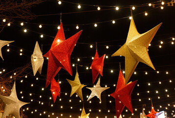 Red and gold five-pointed stars and garlands with light bulbs on the background of the night sky....