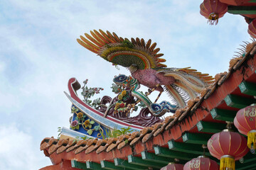 an ornate, traditional Chinese temple with red, gold, and green colors, adorned with pink lanterns, intricate carvings, and a white balustrade under a clear blue sky.