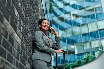 Businesswoman talking on phone with suitcase outdoors