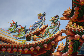 A ornate, multi-tiered Chinese temple with vibrant red and green roofs, detailed eaves, colorful patterns and dragons,  set against a bright blue sky with scattered clouds