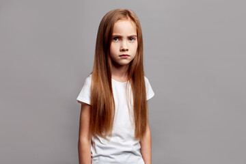 Studio portrait unhappy girl with long hair isolated on neutral background, upset child looking into camera with sad eyes