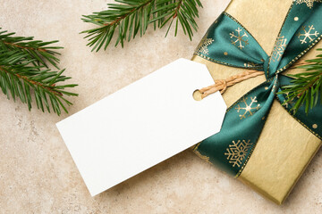 Christmas gift tag mockup with blank tag and elegant gold gift box, adorned with green ribbon and snowflake patterns, featuring natural pine branches for festive ambiance