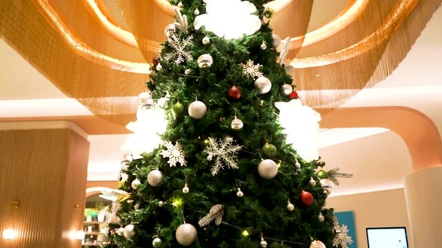 A close-up view of a beautifully decorated Christmas tree featuring silver, red, and green ornaments, sparkling snowflake decorations, and warm festive lighting. The rich green branches