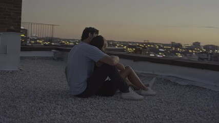 Couple embracing on rooftop at dusk, overlooking city lights