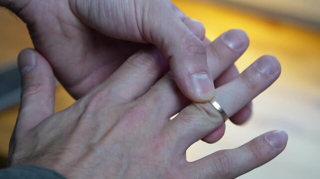 close up of a mans hand sliding a simple thin gold wedding ring onto a finger symbolizing marriage love commitment romance fidelity slow motion video footage