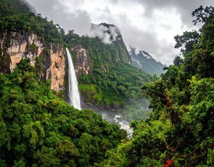 A majestic waterfall cascades down a rocky cliff face, surrounded by lush green foliage and mountain peaks