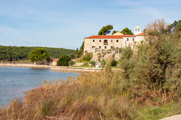 The historic stone Monastery of St. Euphemia stands on a hill overlooking the calm bay, framed by...
