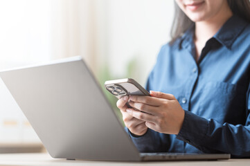 A person using a smartphone while working at a laptop, focusing on browsing and digital communication.Using smartphone social media. Smart phone application. Online shopping smart phone. Search web.