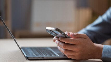 A person using a smartphone while sitting at a workspace, focusing on typing and browsing online.Using smartphone social media. Smart phone application. Online shopping smart phone.Text message phone.