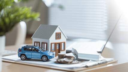 Mini house, car model, coins, and documents on a bright office desk representing finance and...