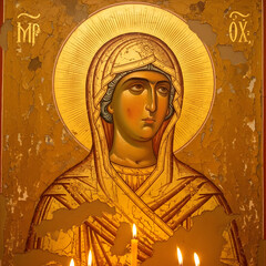 A painted icon depicts a woman with a golden halo, wearing a veil and a long robe, with candles in the foreground.