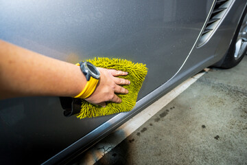 Close-up of a worker's hand washing the side of a car with a yellow hand wash. Cleaning a car in a garage.